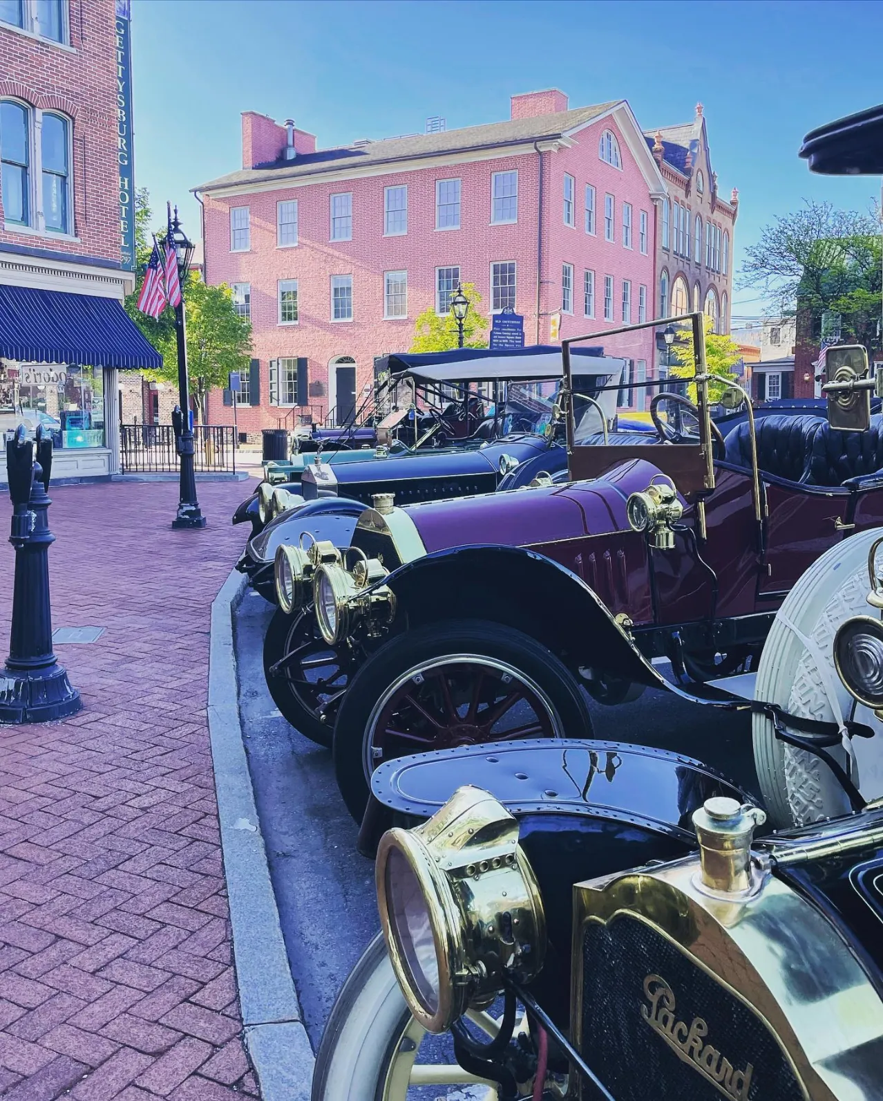 Row of vintage cars parked on a brick street in front of historic buildings