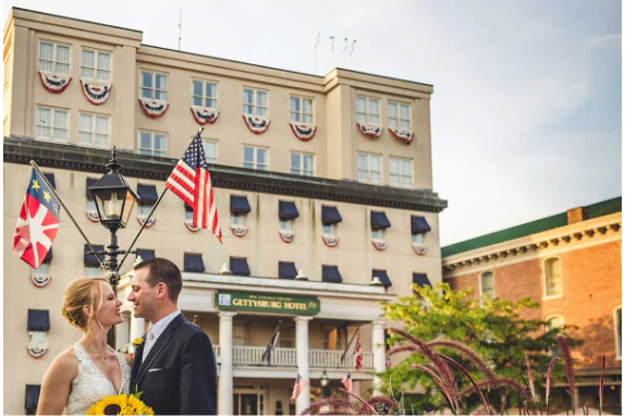 Bride and groom standing in front of the Gettysburg Hotel with American flags in the background.