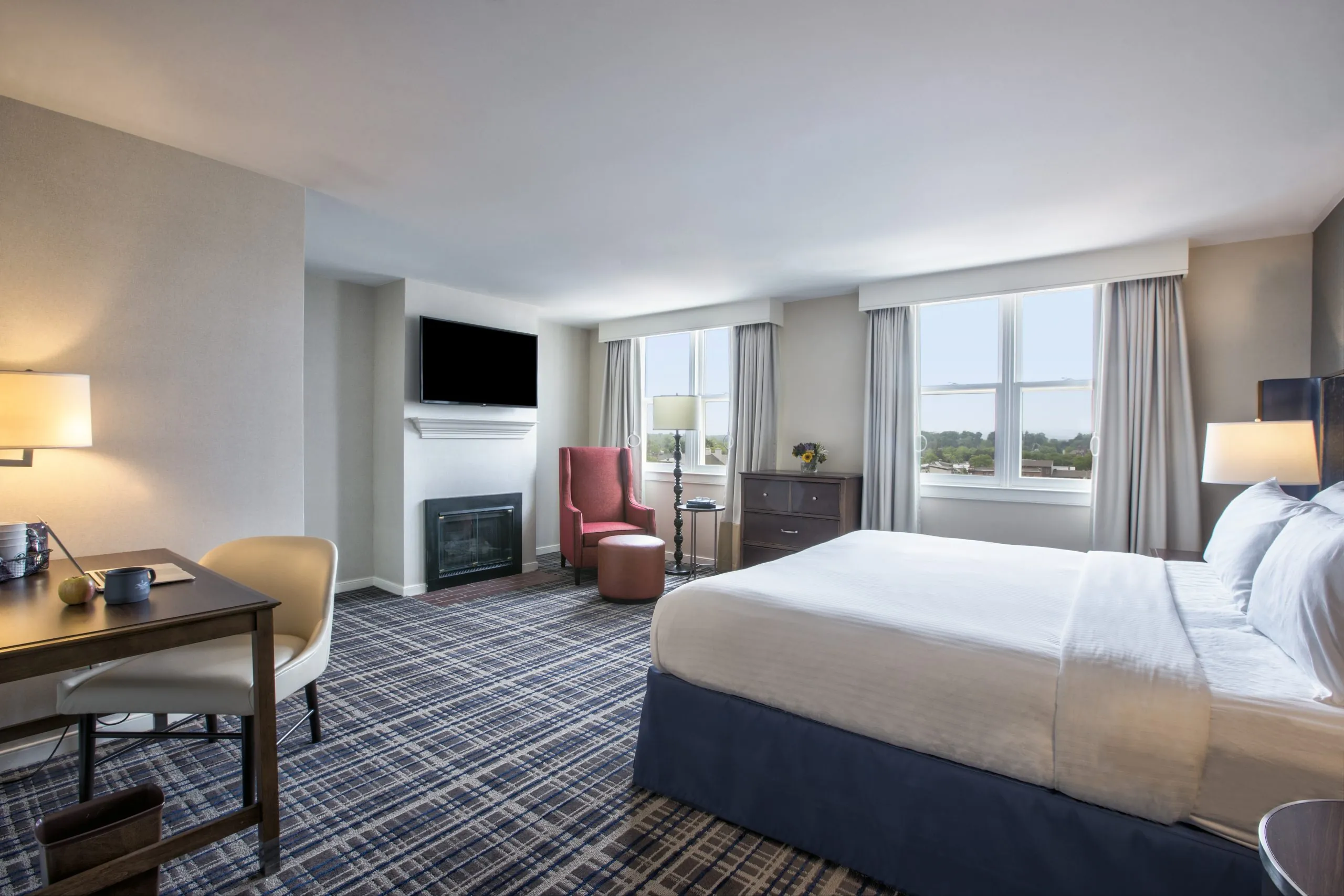 Spacious guest room with a king bed, desk, seating area, and large windows